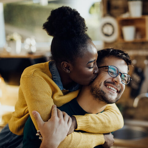 Young African American woman kissing her fiance having fun with him at home.
